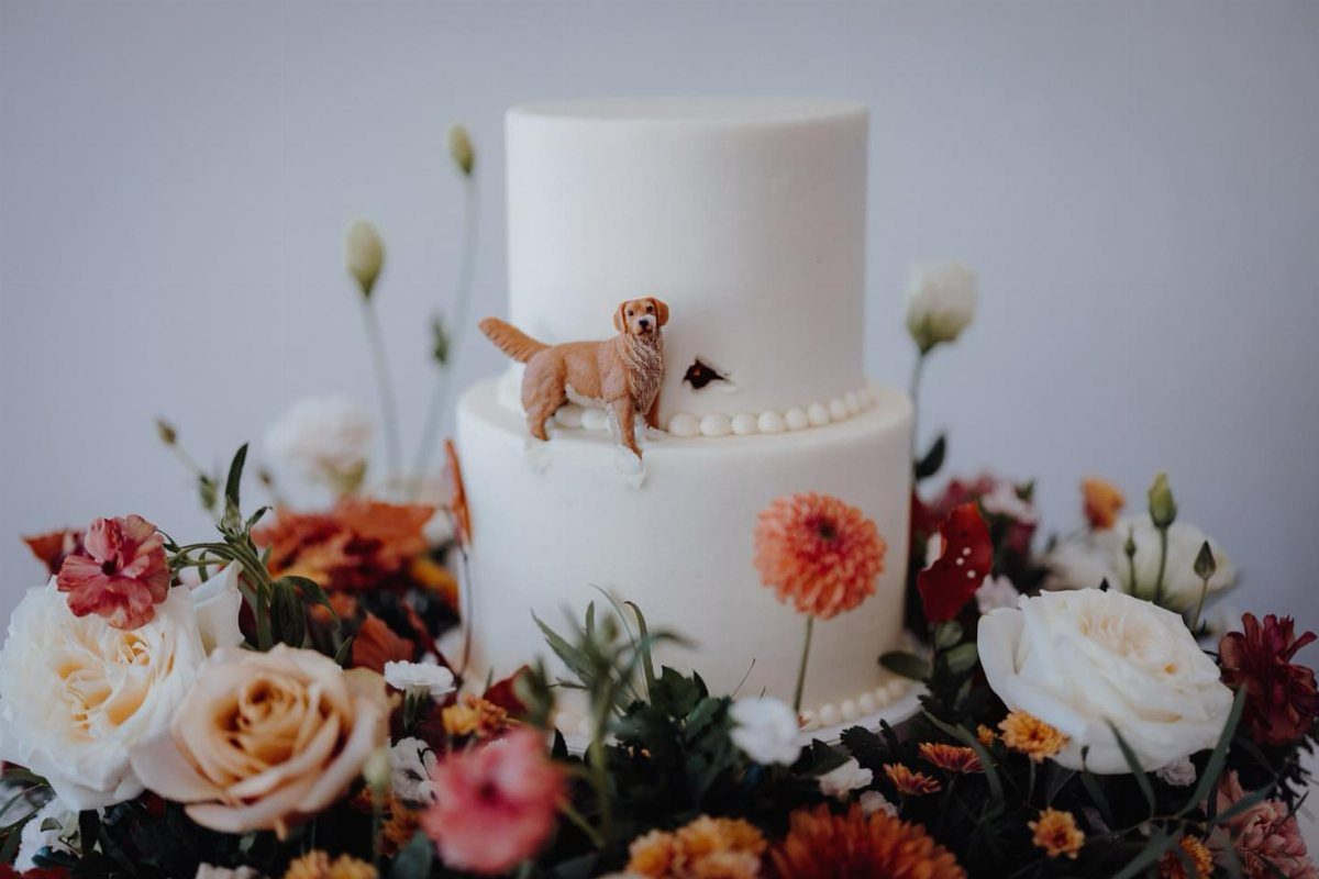 Golden retriever dog figurine on a two-tier white cake surrounded by autumn flowers