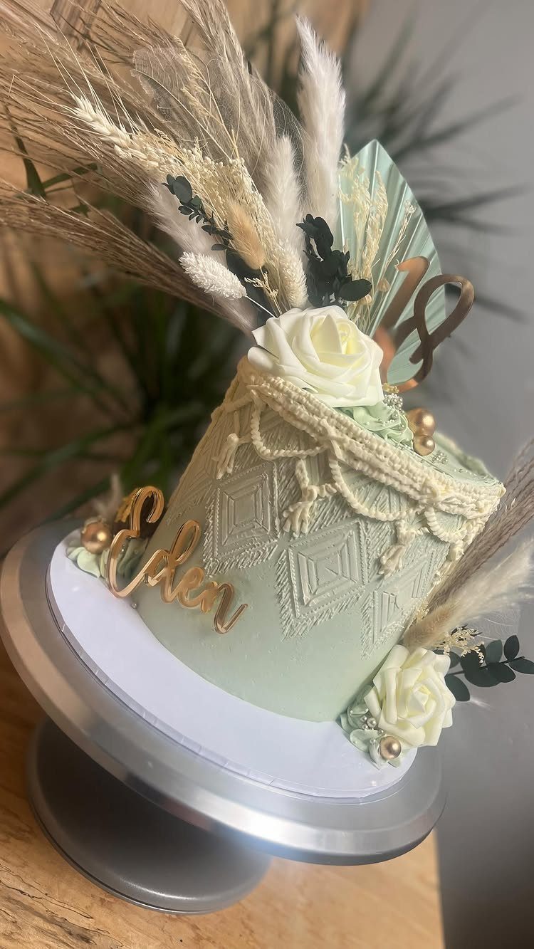 Light green cake with pampas grass topper and macrame-textured frosting and white roses.