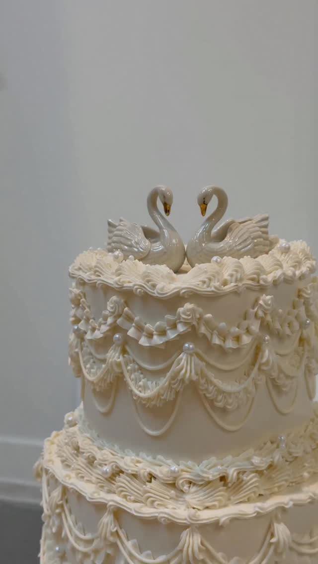 Two white swan figurines acting as a topper on a tiered white cake.