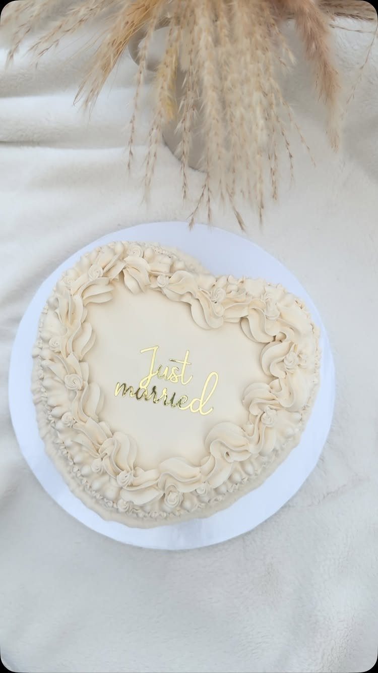 Heart-shaped white cake with a gold Just Married cake topper and piped frosting.