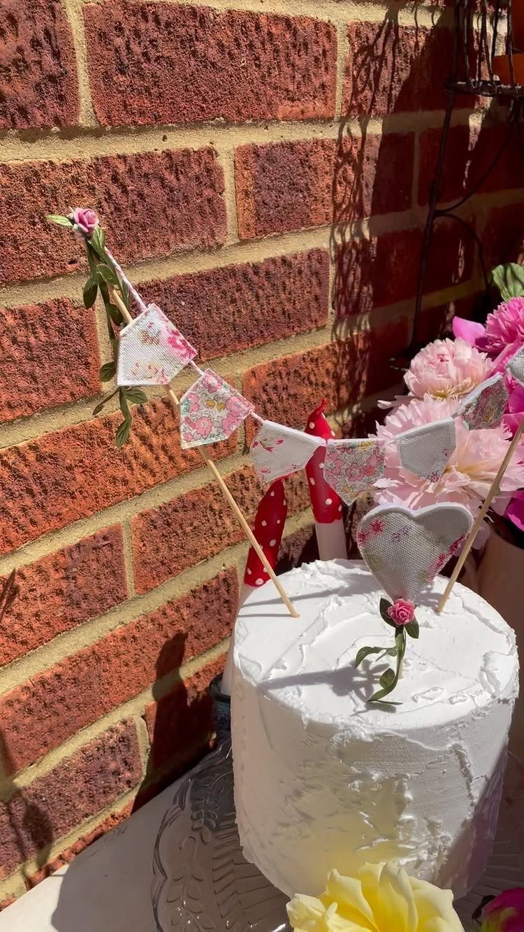 White frosted cake with a mini floral bunting cake topper against brick wall