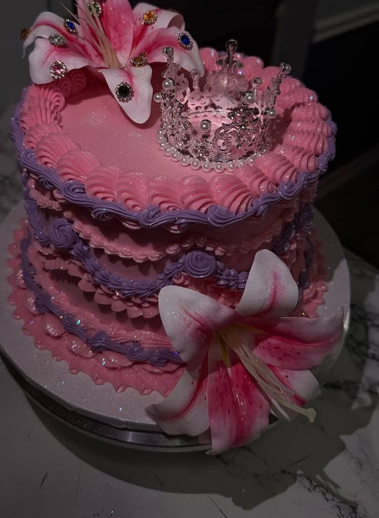 Pink frosted cake topped with a silver tiara and pink lily flowers.