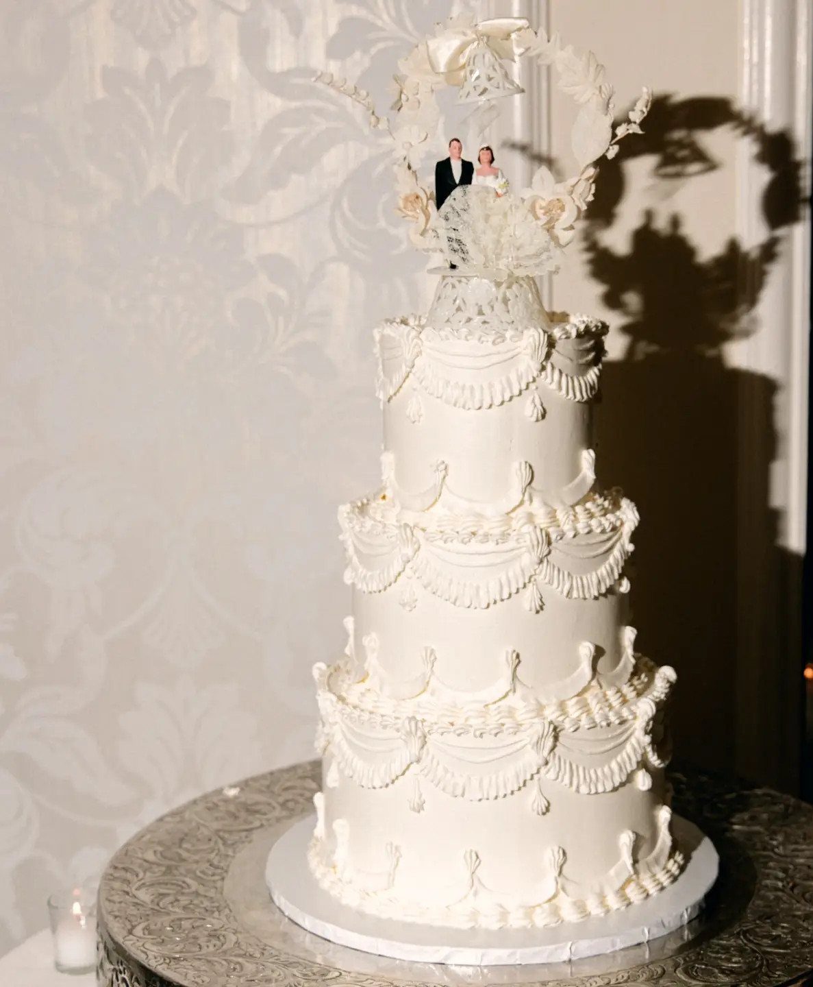 Four-tier white wedding cake topped with a bride and groom figurine in a frame.