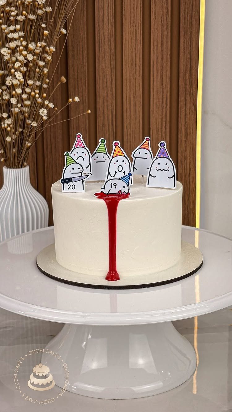 White frosted cake with cartoon ghost cake toppers wearing colorful party hats