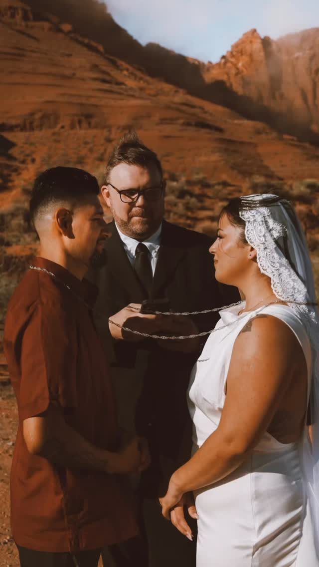 Couple exchanging vows with an officiant in a red rock desert landscape.