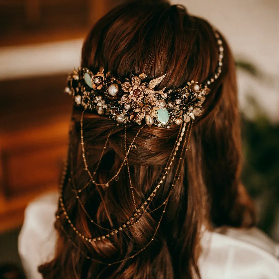 Ornate gold hair accessory with pearls and chains on brown wavy hair.