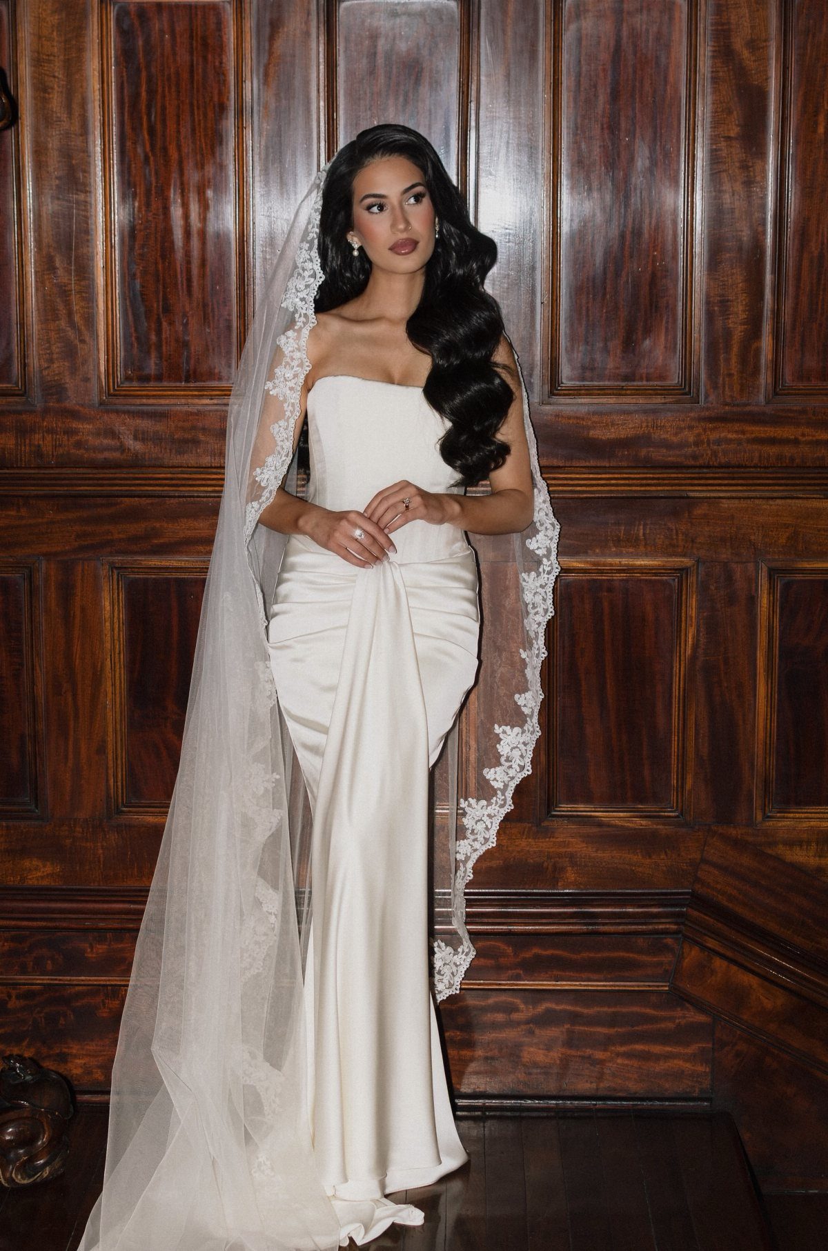 Woman in wedding dress with dark hair styled in side-swept waves and veil.