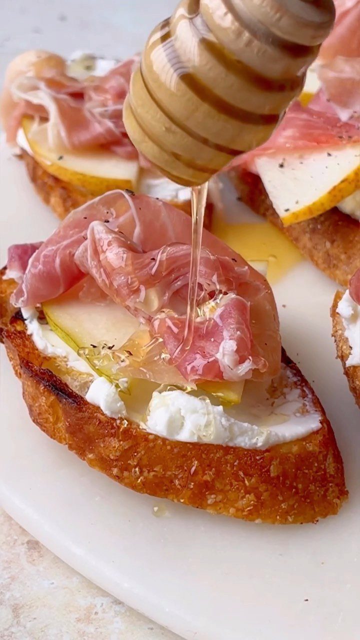 Toasted baguette with cheese, pear, and prosciutto being drizzled with honey.