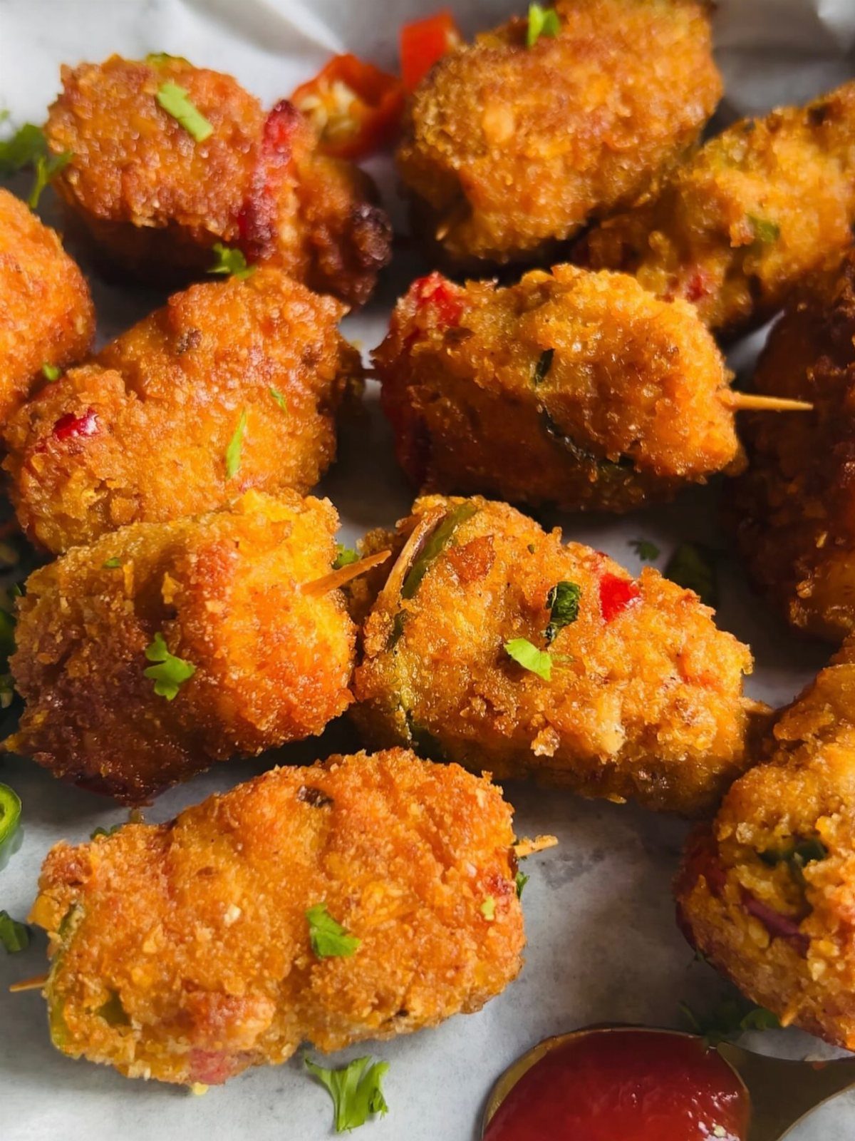 Breaded fried chicken satay skewers garnished with herbs and red pepper bits.