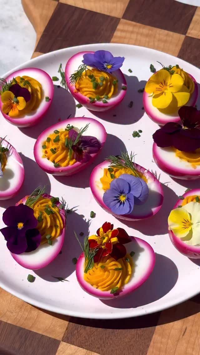 Pink deviled eggs with yellow filling and edible flowers on a white plate.
