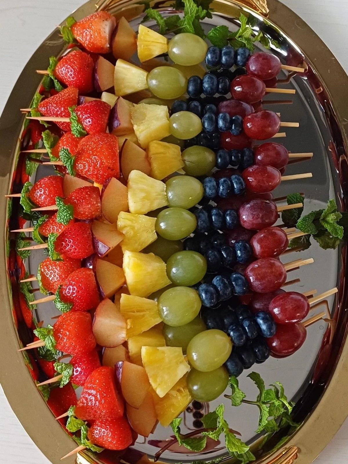Fruit skewers with strawberries, pineapple, grapes, and blueberries on a gold platter.