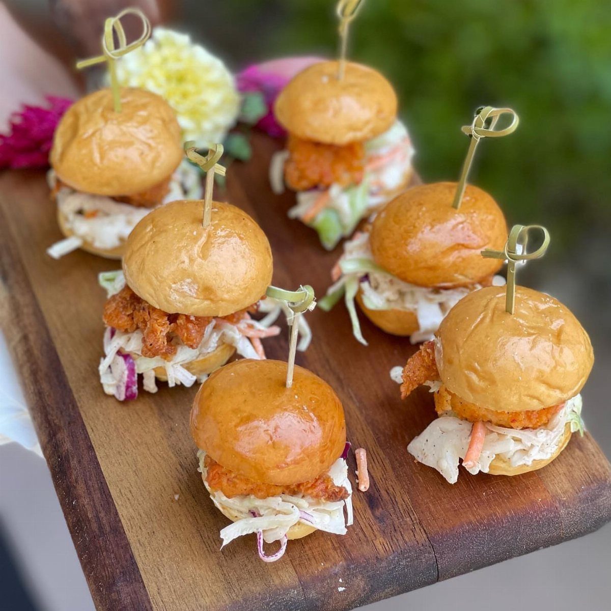 Mini chicken sliders with coleslaw on a wooden board with bamboo skewers.