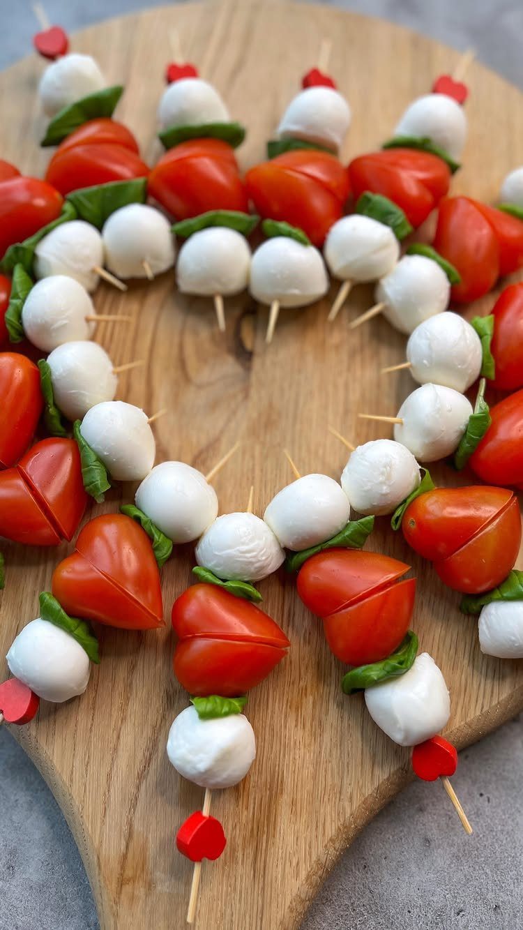 Heart-shaped caprese skewers with mozzarella and basil on a wooden board