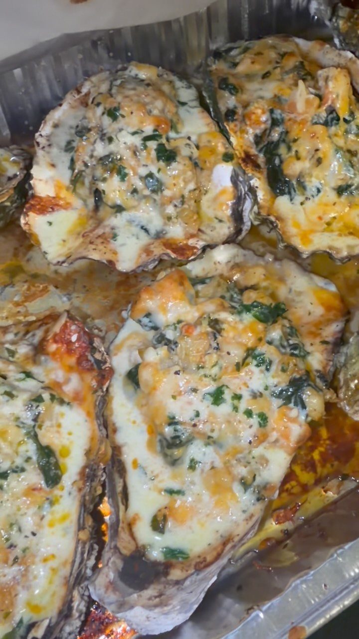 Baked oysters Rockefeller with melted cheese and herbs in a foil pan.