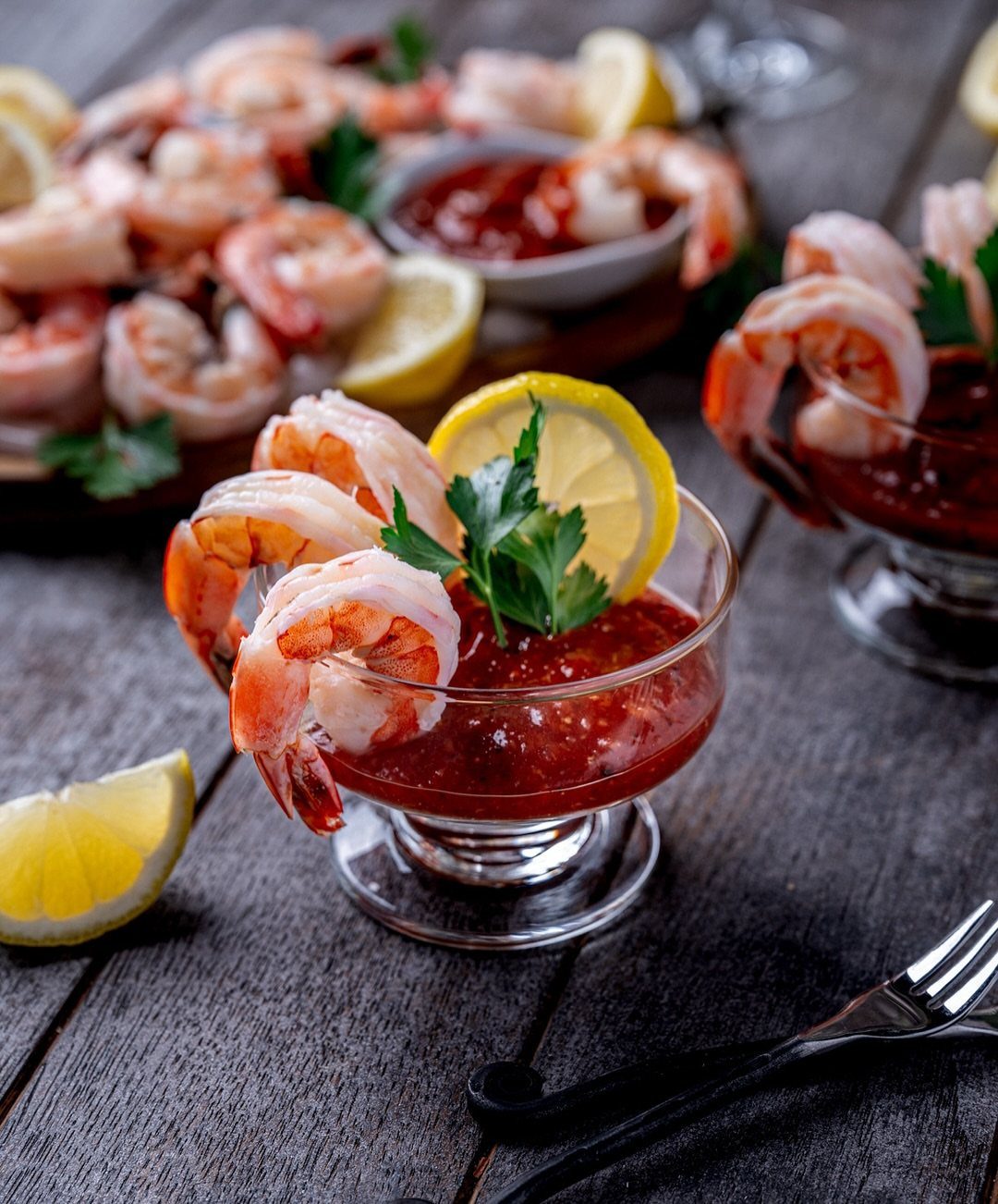 Shrimp cocktail served in glasses with red sauce, lemon slices, and fresh parsley.