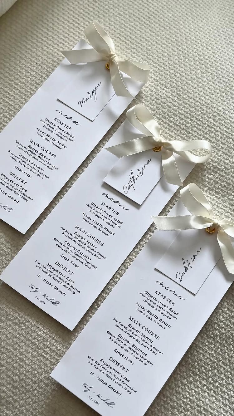 Three white wedding menus with cream satin bows and personalized name tags.