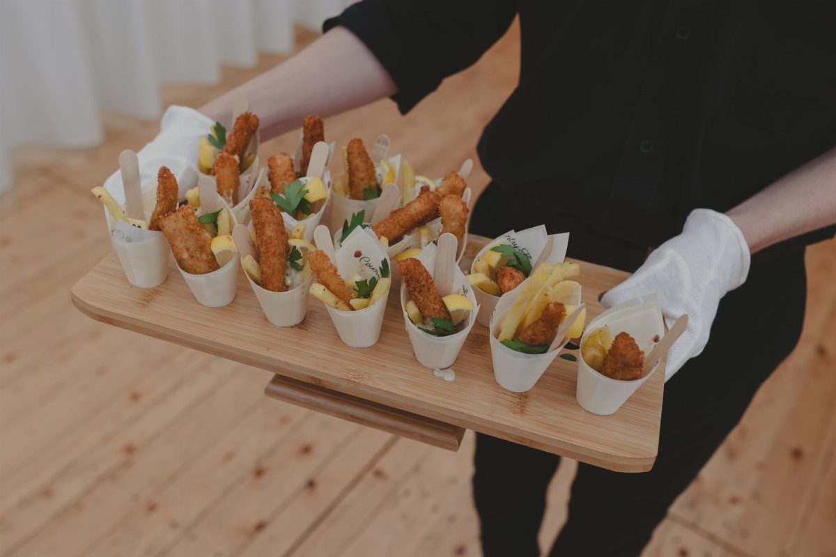 Fried fish and chips served in small white paper cones on a wooden tray.