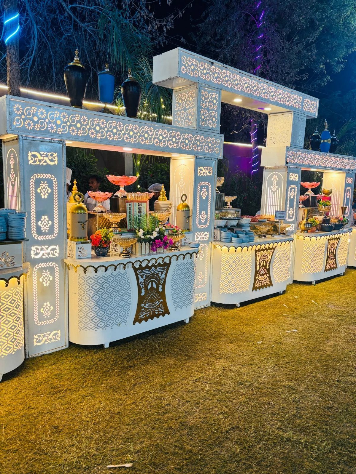 Ornate white carved food stations with gold accents on a grass lawn