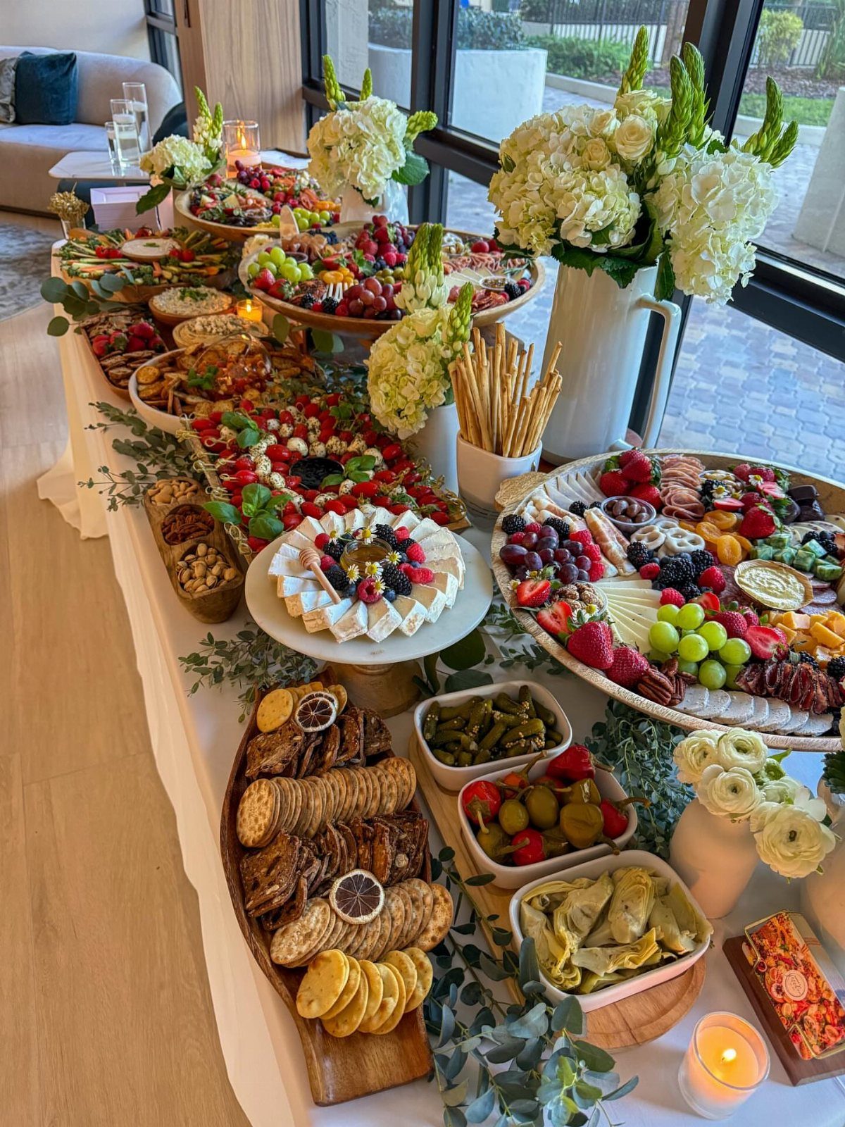 Abundant food spread with cheese, fruit, and crackers on a white wedding table.
