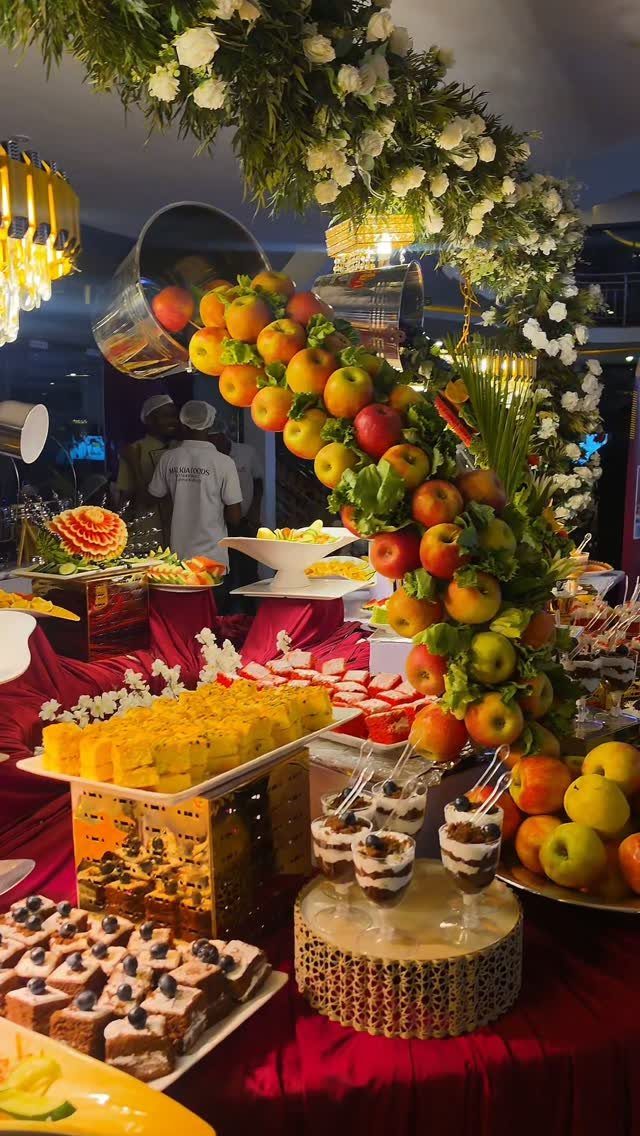 Lavish wedding buffet table with red linens, fruit displays, and floral arch.