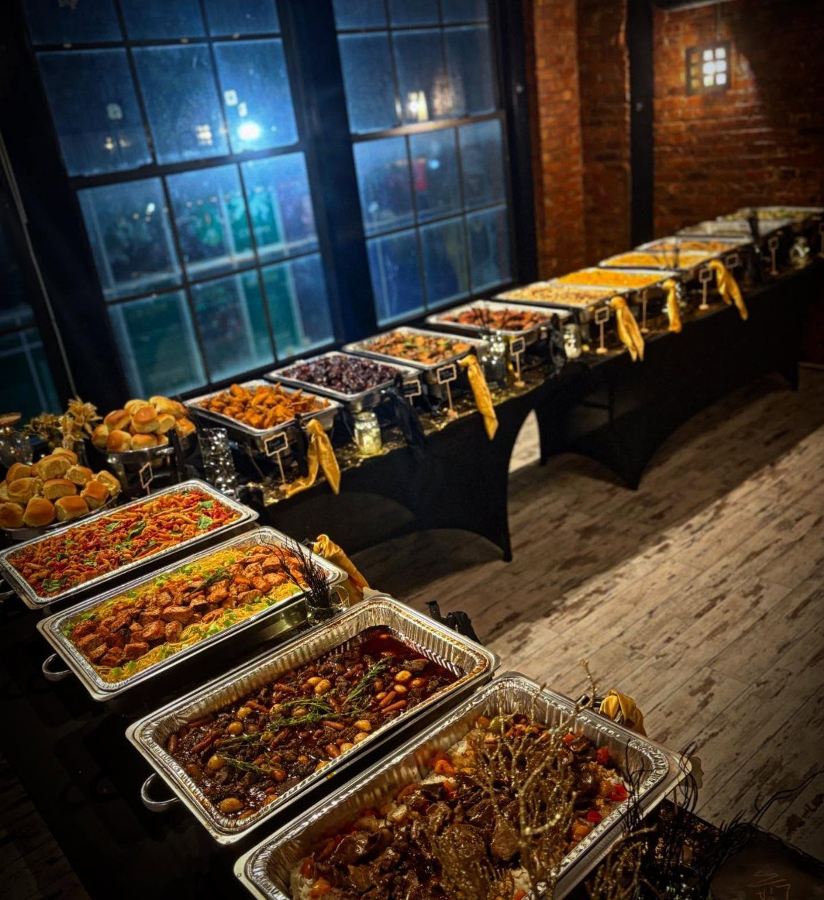 Long buffet line with silver chafing dishes filled with food on black tables.