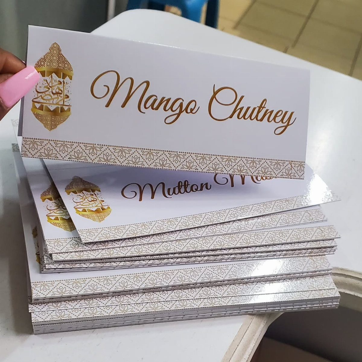 Food labels with gold cursive text for Mango Chutney and Mutton on white cards.