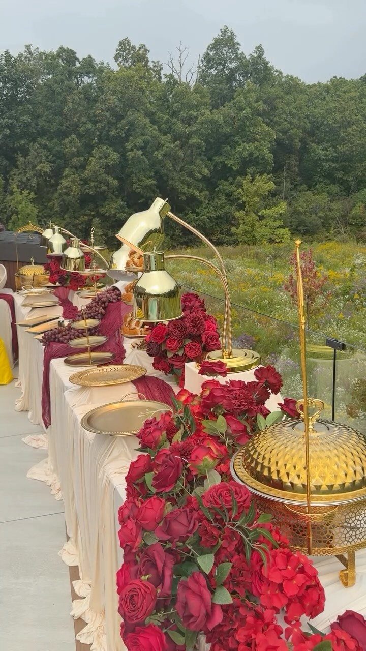 Wedding buffet table with gold serving dishes and lush red rose floral arrangements.
