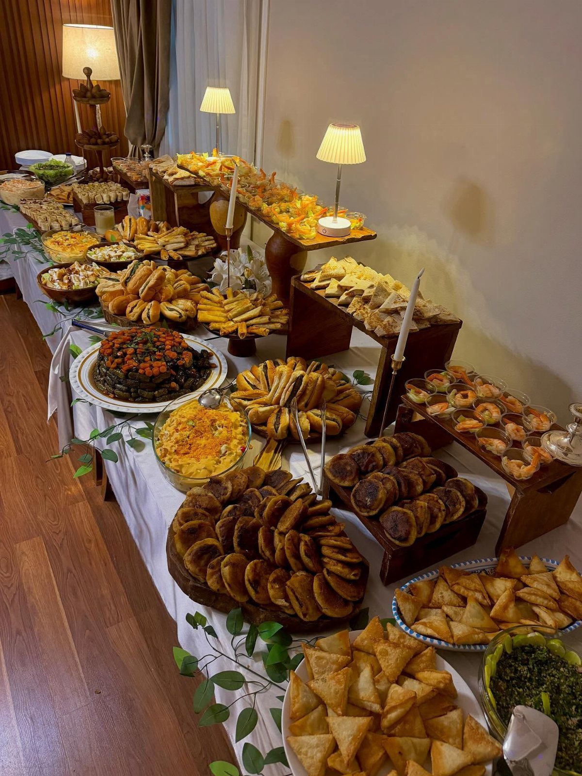 Wedding buffet table with various appetizers and pastries on wooden risers and white linen.
