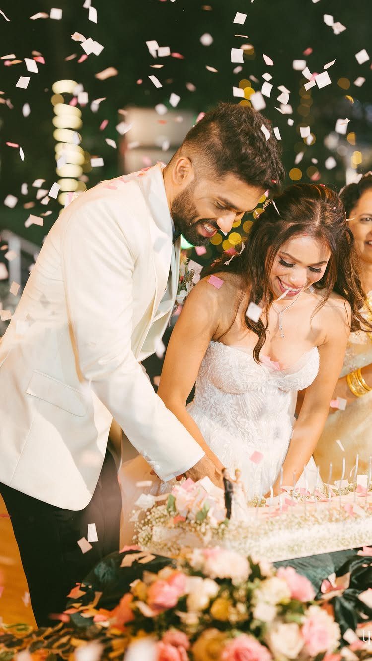 Bride and groom cutting their wedding cake while white confetti falls around them.