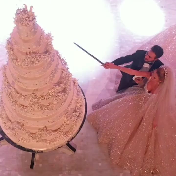 Bride and groom using a sword to cut a giant white wedding cake.