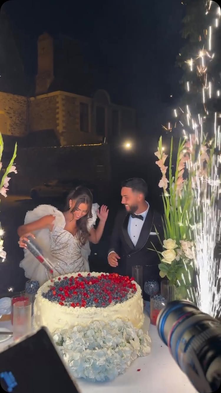 Bride and groom cutting a berry-topped wedding cake with sparklers lighting the night.