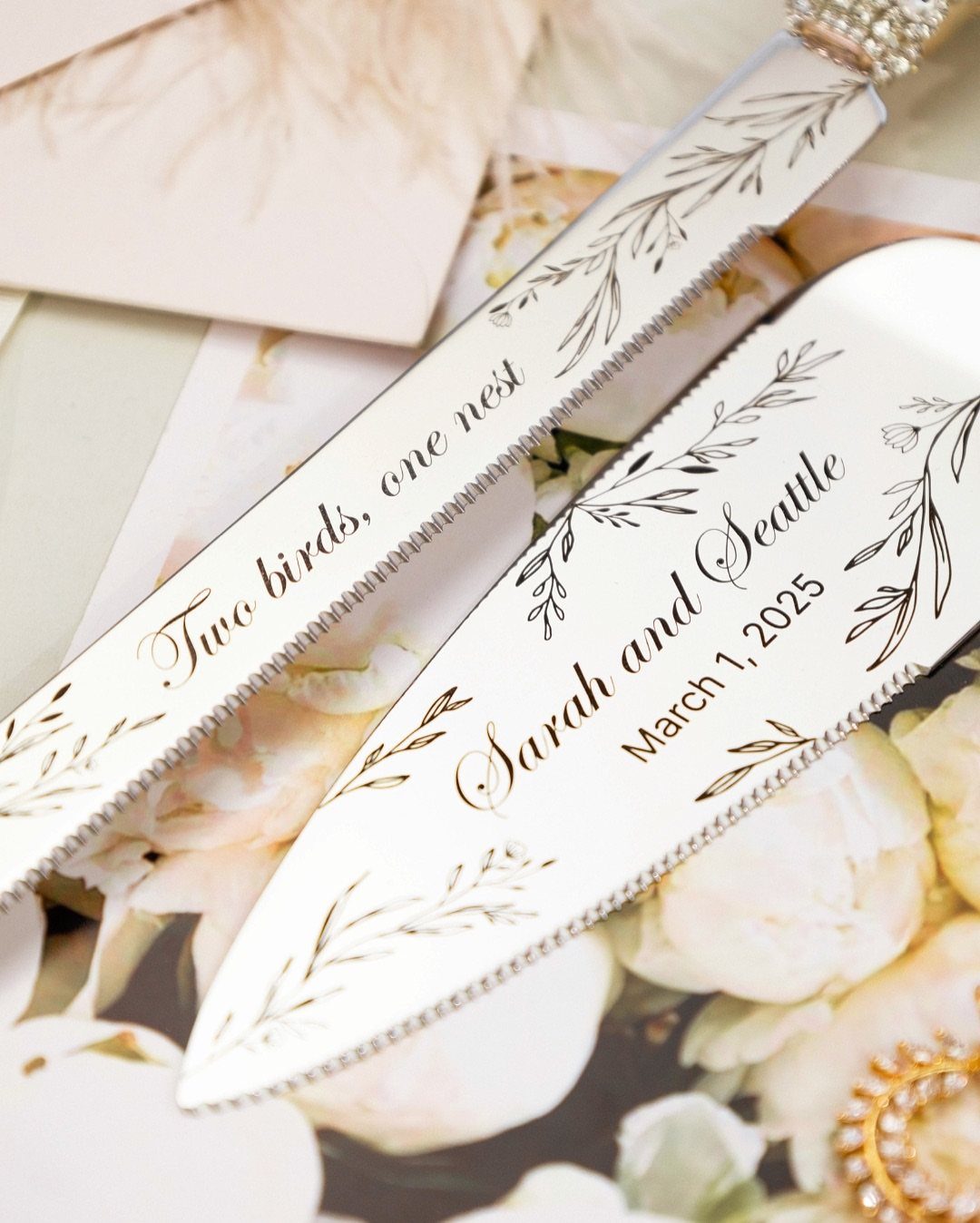 Engraved silver cake knife and server set resting on floral stationery.