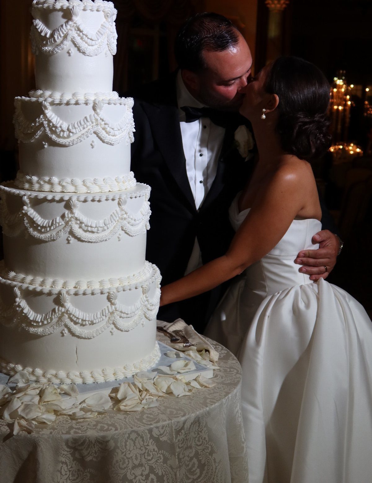 Bride and groom kissing next to a four-tier white wedding cake on a table.