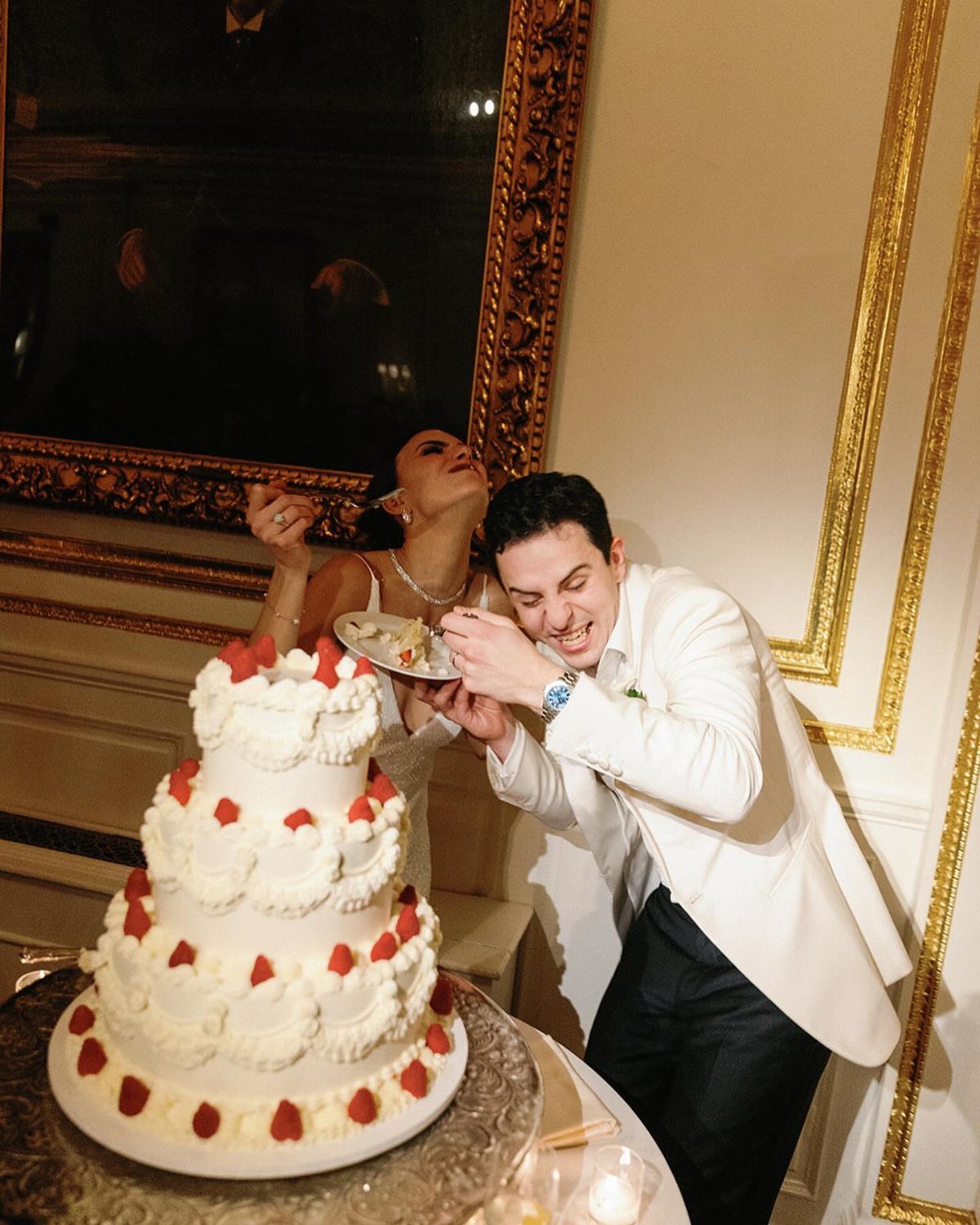 Bride and groom laughing while holding a slice of three-tier strawberry wedding cake.