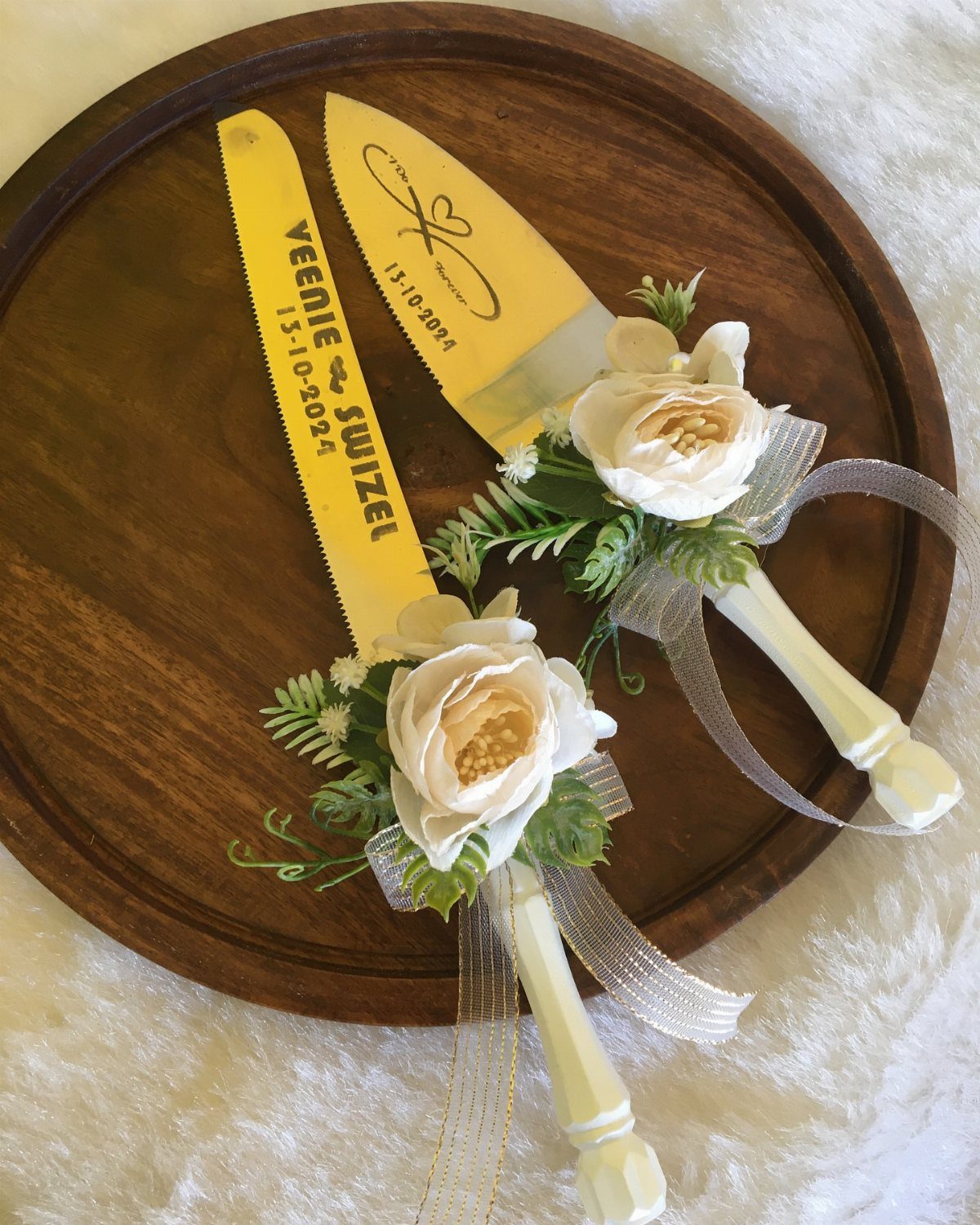 Gold serrated cake knife and server with white floral accents on wooden tray