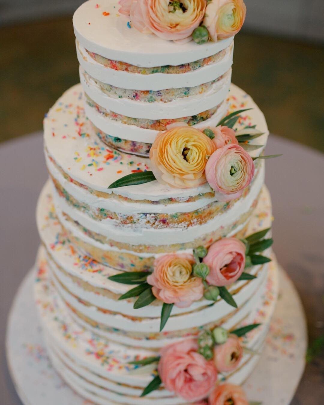 Four-tier confetti sponge wedding cake with semi-naked frosting and fresh pink ranunculus flowers.