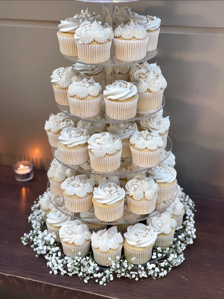 Cupcake tower with white frosting and pearls surrounded by baby's breath flowers