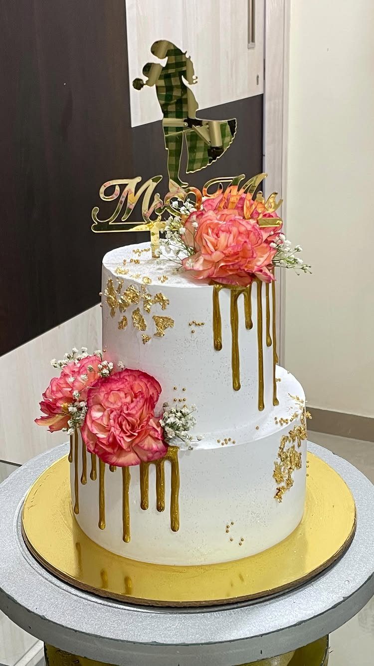 Two-tier white wedding cake with gold drips, pink flowers, and Mr and Mrs topper