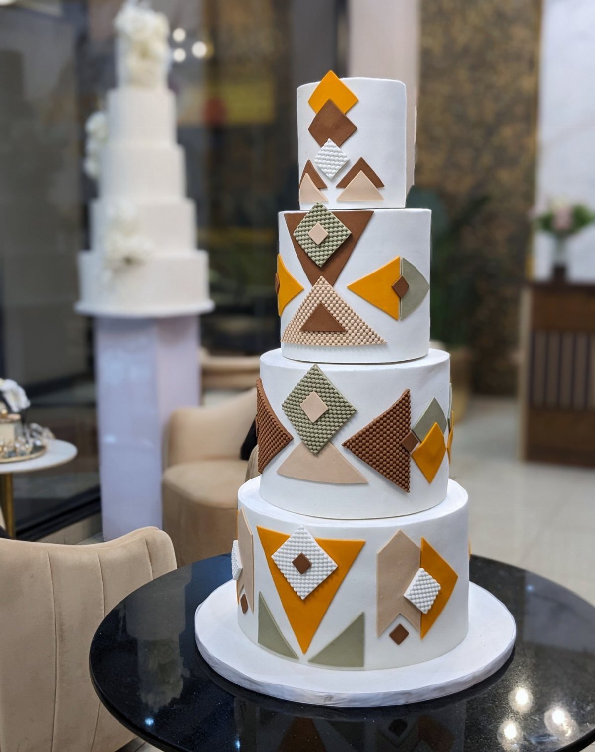 Four-tier white wedding cake decorated with mustard yellow and brown geometric shapes.