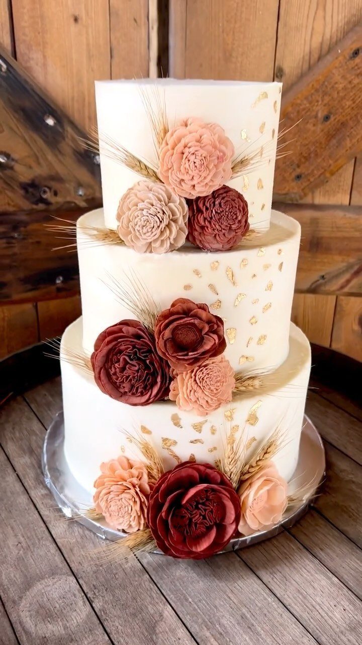 Three-tier white wedding cake with burgundy and peach flowers and dried wheat stalks.