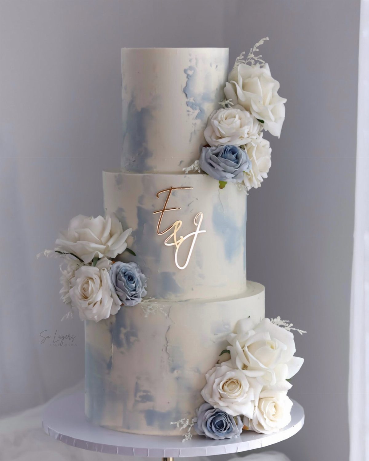 Three-tier white wedding cake with blue watercolor icing and white and blue roses.