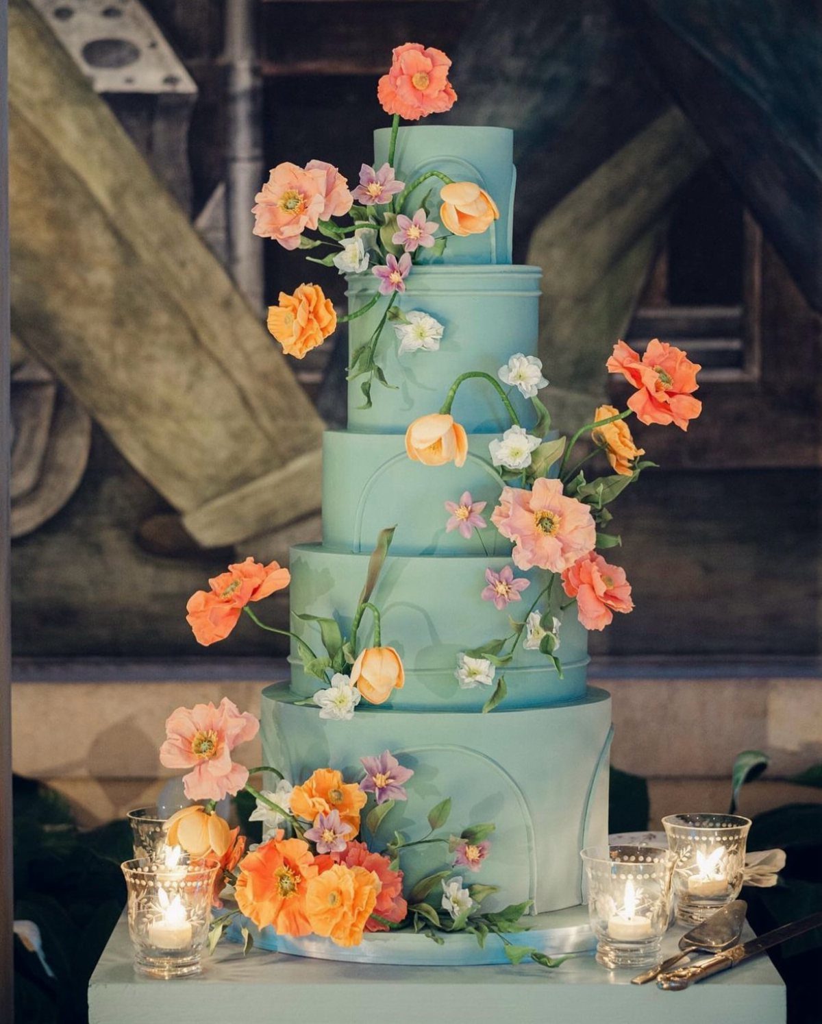 Five-tier light blue wedding cake adorned with colorful orange and pink sugar flowers.