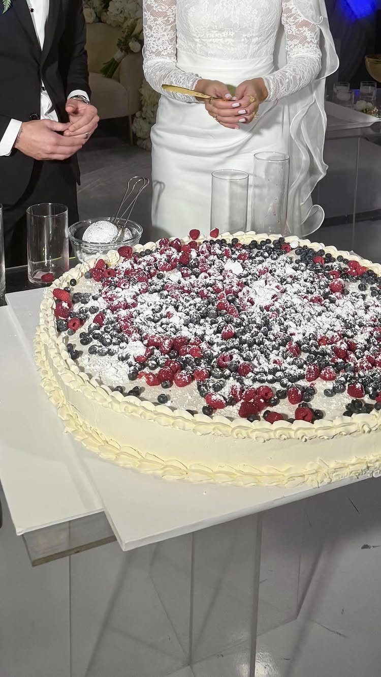 White frosted cake topped with fresh blueberries and raspberries at a wedding reception.