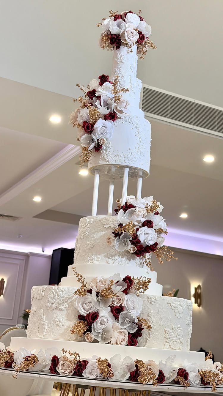 Multi-tiered white wedding cake with red and white roses and gold accents.