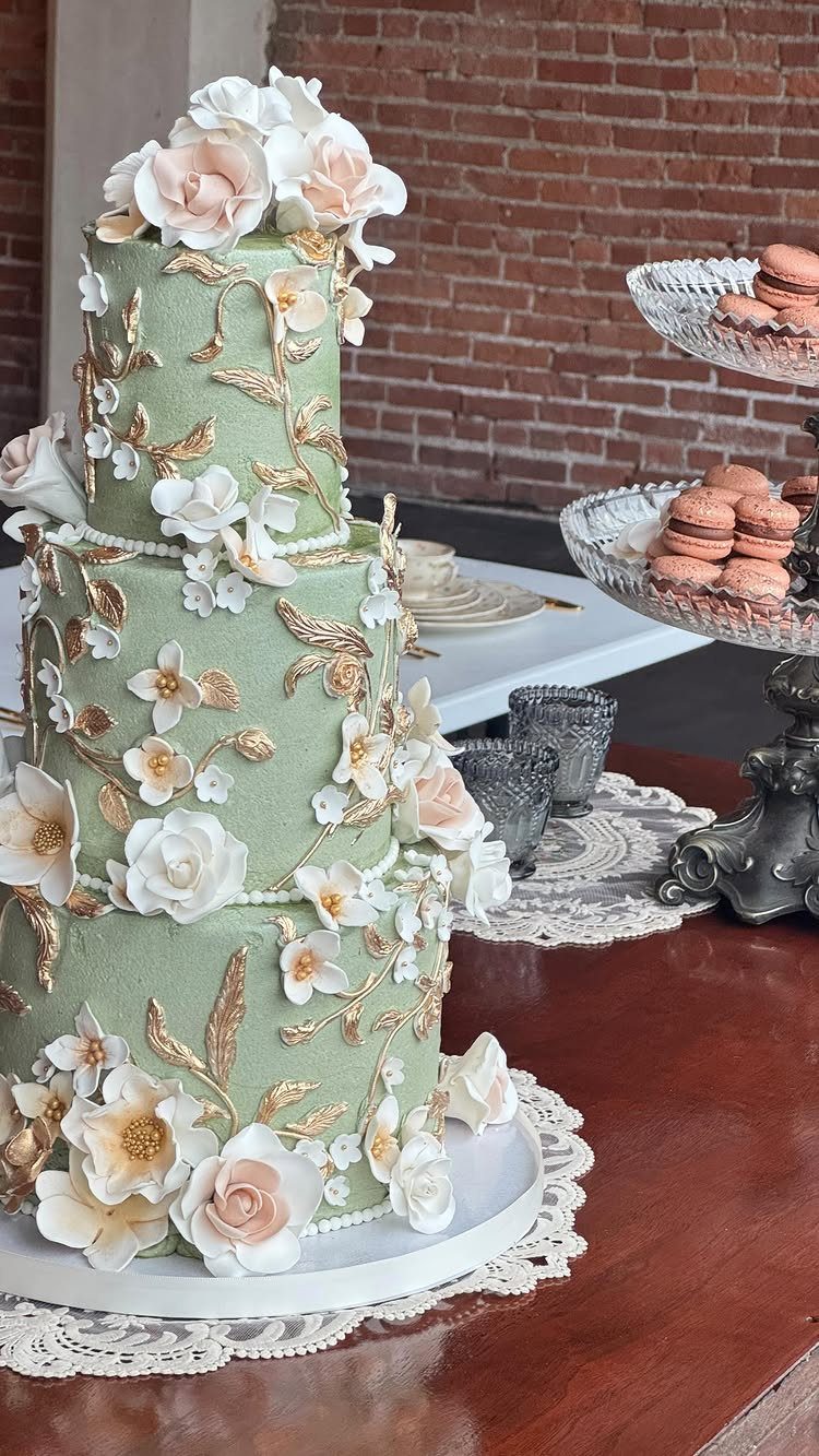 Three-tiered sage green wedding cake with white sugar flowers and gold leaf accents.