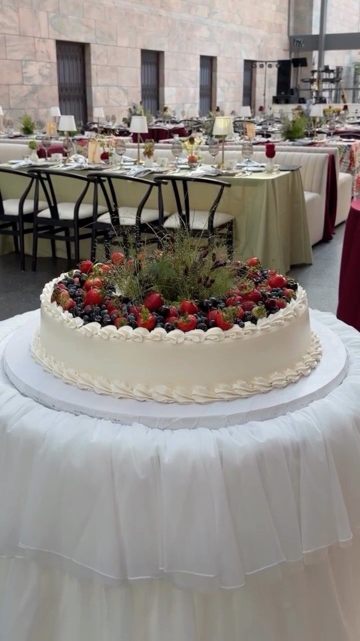 White frosted cake topped with fresh strawberries, blueberries, and greenery on a table.