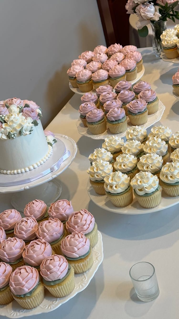 White floral wedding cake surrounded by platters of pink and white cupcakes.