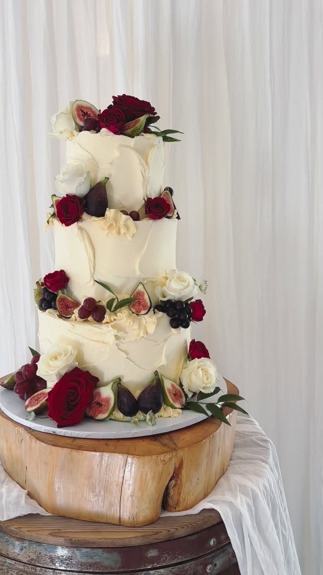 Three-tier white wedding cake decorated with red roses, white roses, and fresh figs.