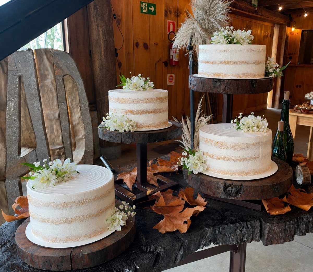 Three semi-naked white cakes with flowers on wooden slabs and autumn leaves.