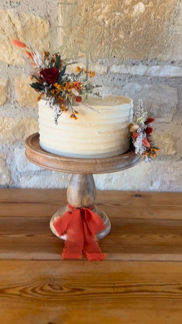White frosted cake with autumn flowers on a wooden stand with red ribbon.